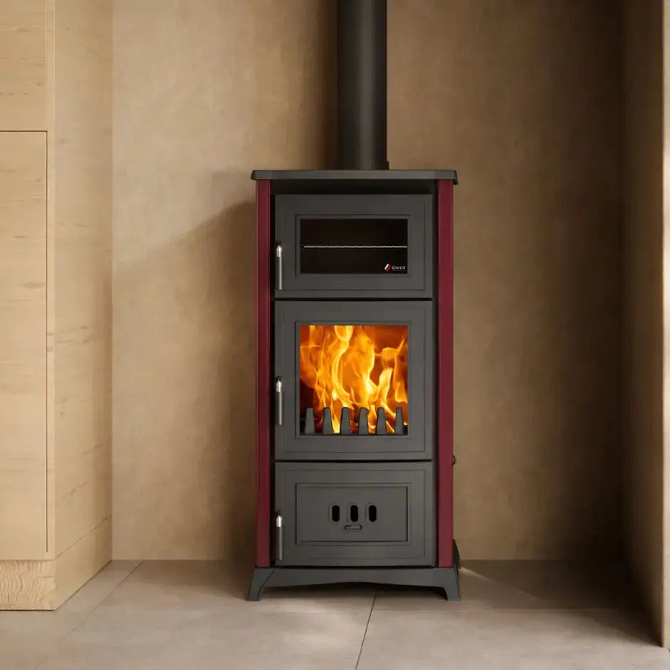 A freestanding black wood-burning stove with a visible orange fire inside, set against a beige wall in a modern interior with light wood cabinetry and a plant.