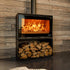 A modern black wood-burning fireplace with a visible fire, set against a rustic wood-paneled wall in a cozy living room with a stone accent wall, staircase, and a quilted sofa.