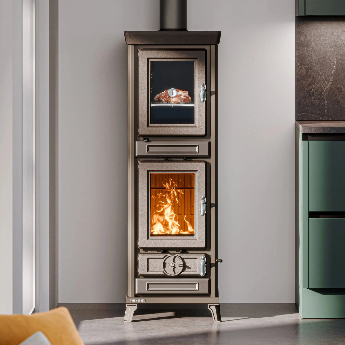 A tall, narrow wood-burning stove with two visible fire compartments, shown standing indoors against a light gray wall. The lower compartment has an open fire, and the upper compartment shows a cooked food dish in a glass window.