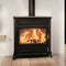A black wood-burning stove with a visible fire inside, set against a white wall and light wood floor.