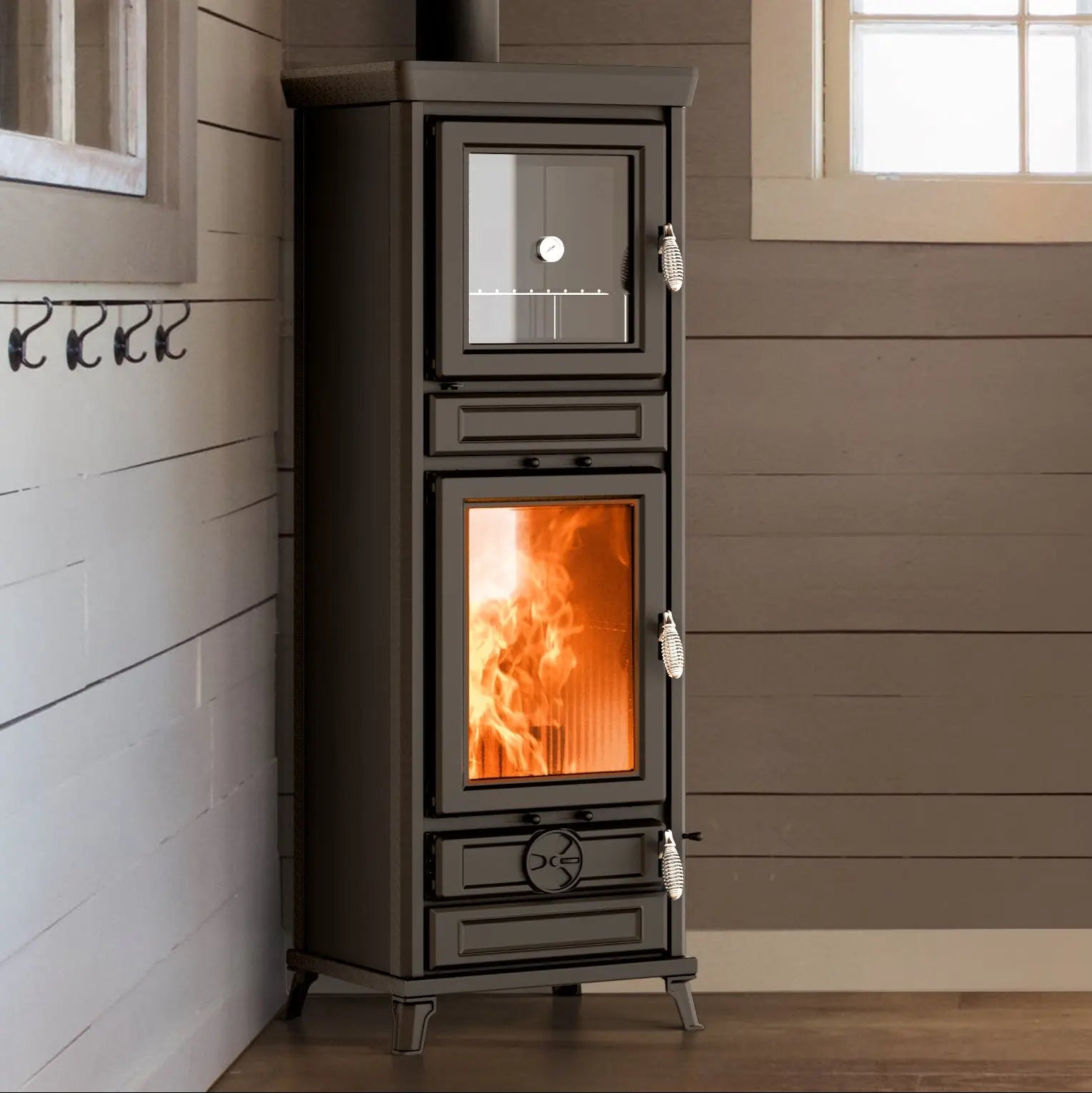 A tall black wood-burning stove with a glass door showing a bright orange fire, set against a brown paneled wall in an indoor room.