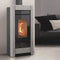 A modern freestanding wood-burning fireplace with a textured gray stone frame and a visible orange flame, shown in a living room setting next to a dark gray sofa.