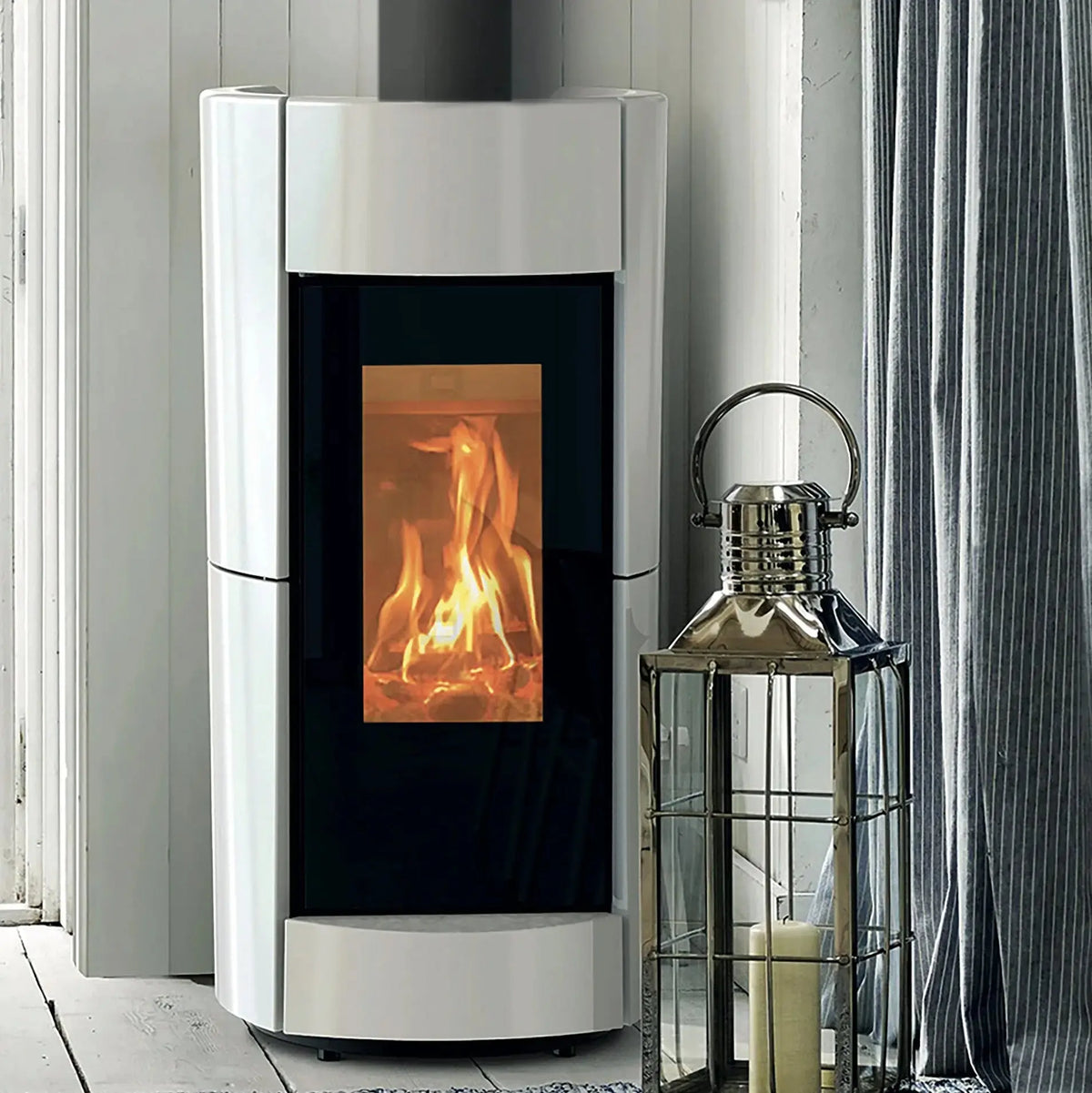 Modern white fireplace with visible flames, next to a decorative lantern in a room with striped wallpaper.