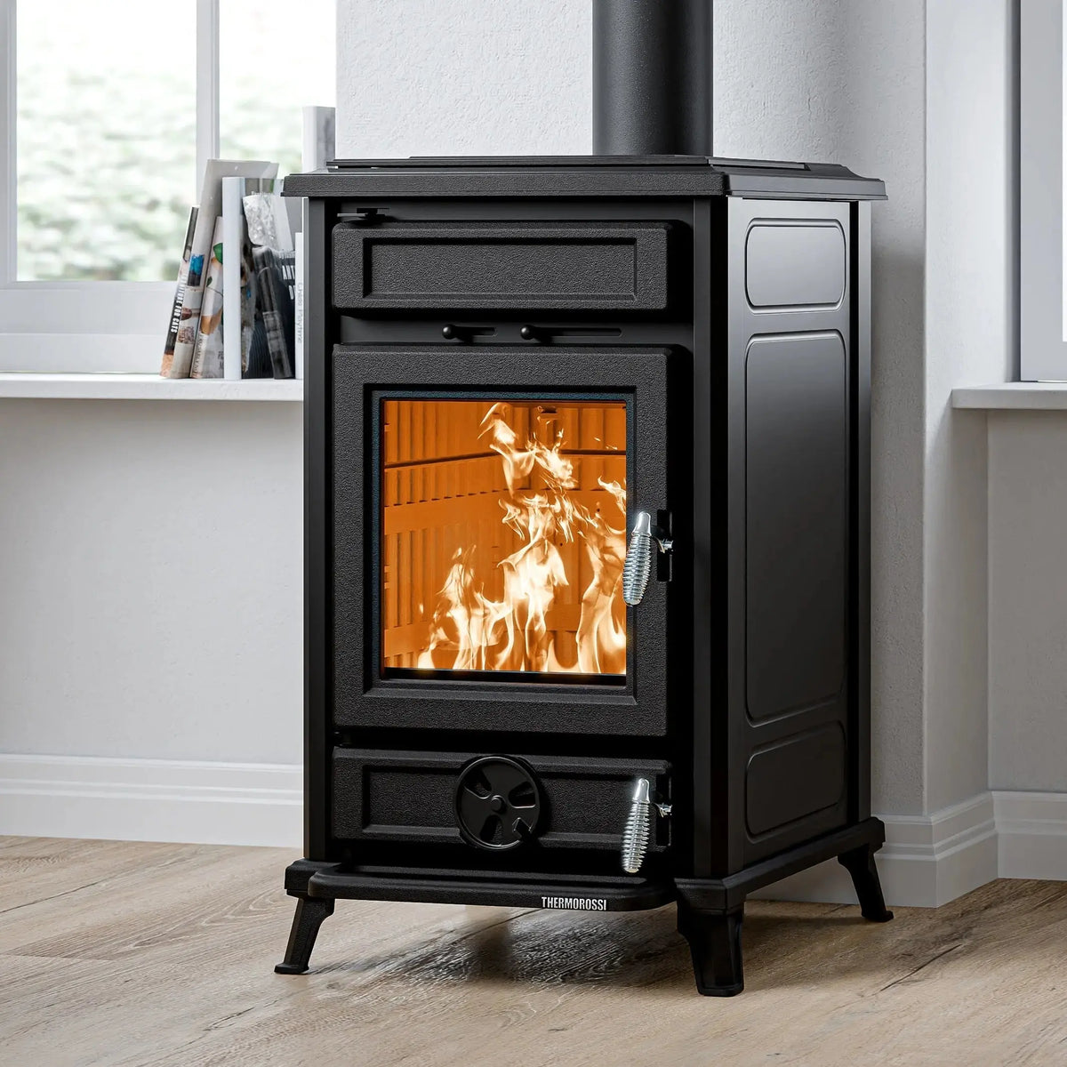 A black wood-burning stove with an open door showing a warm orange fire inside, set in a room with light wood floors and a white wall.