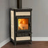 A freestanding black and cream wood-burning stove with a visible fire inside, photographed in a room corner with gray walls and a wood floor.