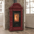 A burgundy freestanding wood-burning stove with a black glass door showing a fire, set against a stone wall in a room with wooden floors and a white door.