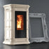 A beige freestanding wood-burning stove with a black glass door showing a glowing fire, photographed indoors against a dark gray wall. A large ornate white picture frame leans against the stove as a prop.