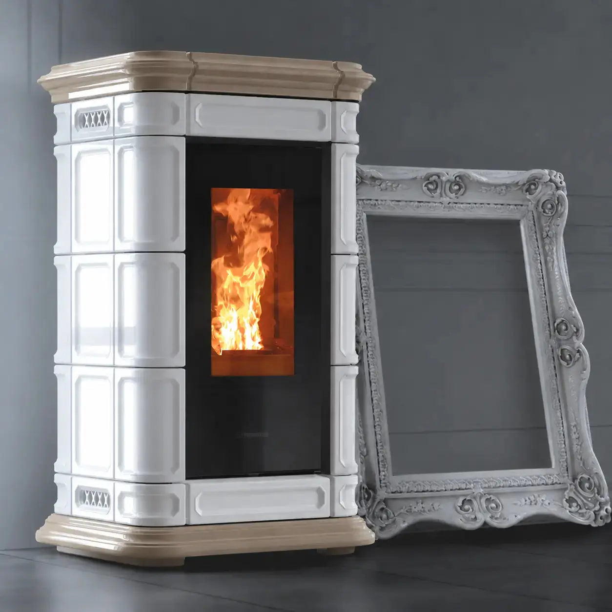 A white and down freestanding wood-burning stove with a black glass door showing a glowing orange fire, photographed against a dark gray wall. An ornate white picture frame leans against the stove.