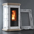 A white and down freestanding wood-burning stove with a black glass door showing a glowing orange fire, photographed against a dark gray wall. An ornate white picture frame leans against the stove.