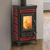 A freestanding wood-burning stove with a black cast iron body and red tile fronts, shown standing on a wood floor against a light wall with a fire visible through the glass door.